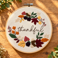Autumn Thankful finished embroidery hoop: the word thankful in script inside a wreath of autumn leaves, acorns and berries, 7 inch wooden hoop on a woodgrain table